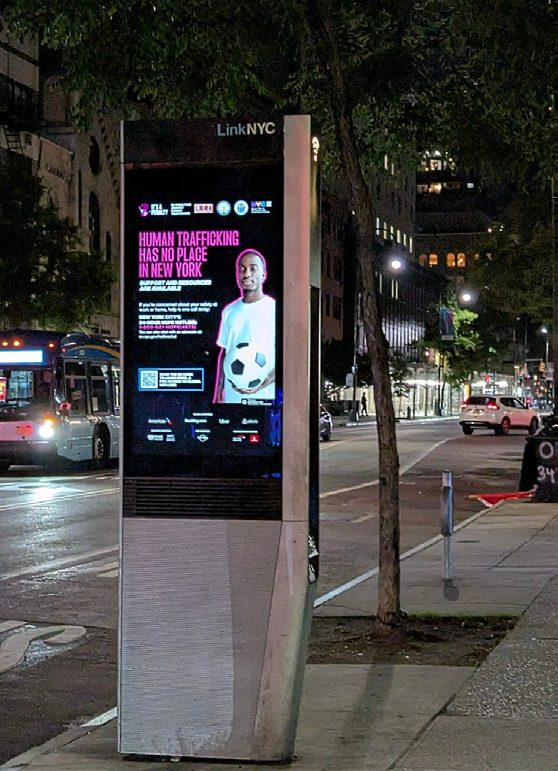 Campaign artwork on a LinkNYC street kiosk at night